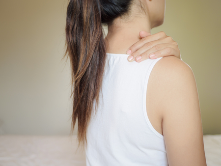 Beautiful asian woman suffering shoulder neck pain, tired sit on bed background with back view. Health care and medical concept.の写真素材