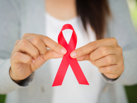Woman hand holding red ribbon HIV, world AIDS day awareness ribbon.  Healthcare and medicine...
