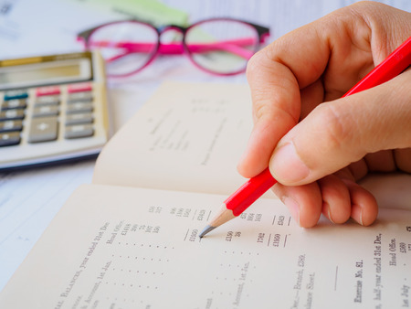 Closed up woman hand using calculator with note book and red pencil  in white background.の写真素材
