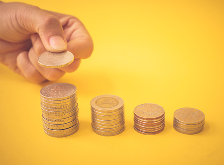Abstract money saving. Hand put money coins to stack of coins on yellow background.の写真素材
