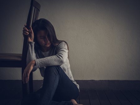 Depressed woman sitting on the floor nearby a chair in dark room at home. Lonly , sad, emotion concept.の写真素材