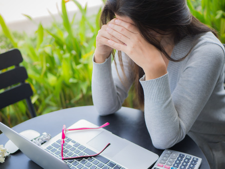 Young asian woman headache while sitting in a cafe garden with her laptop,  Stressful for work.