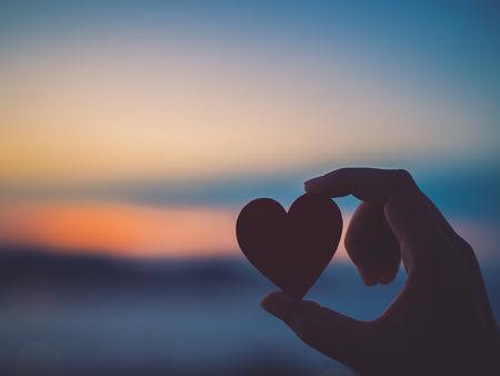 Silhouette hand holding beautiful heart during sunset background. Happy, Love, Valentine's day idea, sign, symbol, concept.の写真素材