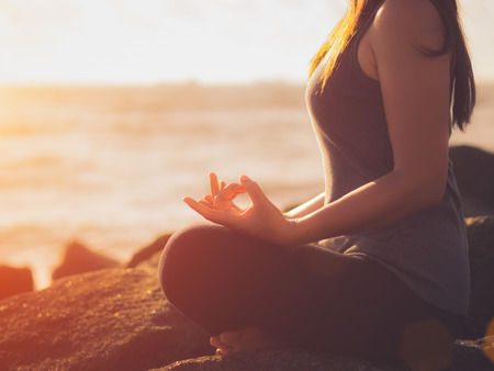 Yoga concept. Closeup woman hand practicing lotus pose on the beach at sunsetの写真素材