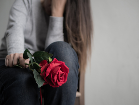 Sad woman sitting and crying with red rose in her hand. Lonly , love, emotion concept.の写真素材