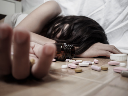 Young woman is lying on the floor with a lot of pills. Overdose and concept.の写真素材