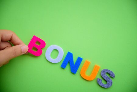Abstract hand arrange BONUS alphabets word on green background. Business achievement concept.の写真素材