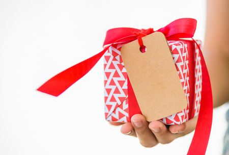 Woman hand holding a red gift box with tags card copy space on white background.の写真素材