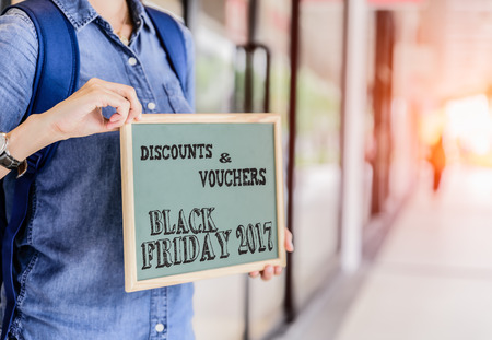 Woman holding a board with the text Black Friday in the shopping mall background.