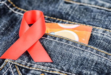 Condom pack and red awareness ribbon on blue jeans pocket. AIDS and HIV awareness concept.