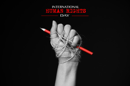 Hand with red pencil tied with rope, depicting the idea of freedom of the press or freedom of expression on dark background in low key. International human rights day concept.の写真素材