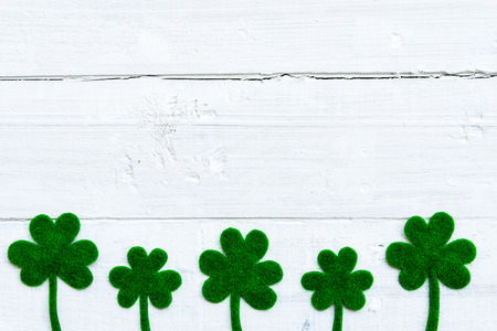 Happy St Patricks Day message and a lot of green paper clover leaf on white wooden background