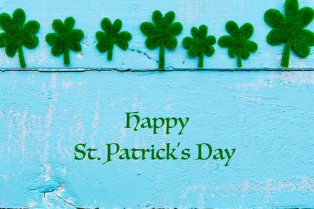 Happy St Patricks Day message and a lot of green paper clover leaf on Pastel white and blue wooden table background texture.の写真素材