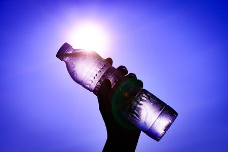 Silhouette of closeup Woman's hand holding plastic water bottle over sunlight effect. World Water Day concept.の写真素材