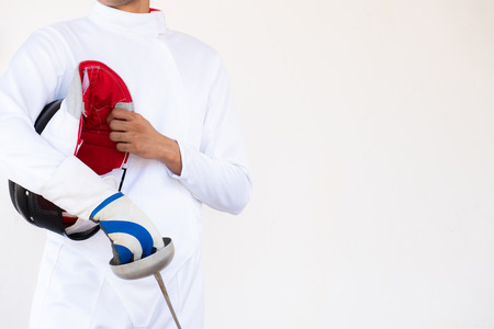 Close-up of a fencer in white fencing suit and holding his mask and a sword on white background