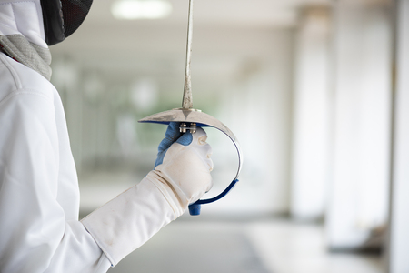 Close-up of a fencer in white fencing suit and holding her sword. Sport and recreation concept.