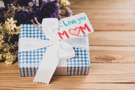 Happy mother's day concept. Gift box with flower, paper tag with Love you MOM text on wooden table background.の写真素材
