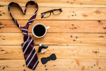 Happy fathers day concept. Top view of father's accessories coffee, retro camera, paper mustache, red tie in heart shape with Love DAD and gift box on wooden table background.の写真素材