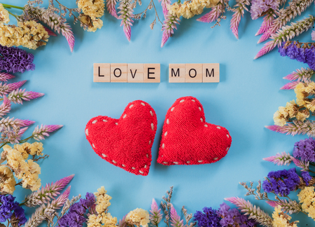 Happy mother's day concept. Top view of two handmade red heart with flower, wooden block with Love Mom text on pastel blue background.の写真素材