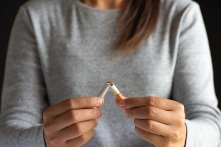 World No Tobacco Day. STOP Smoking. Close up woman hand breaking, crushing or destroying cigarettes on black background.の写真素材