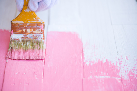 Close up woman hand holding brush painting pink color on a white wooden tableの写真素材