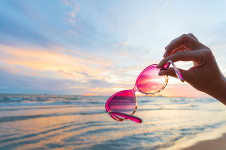 Soft focus on woman hand holding sunglasses over sea and Sandy beach in background during sunset for summer holiday and vacation concept.の写真素材