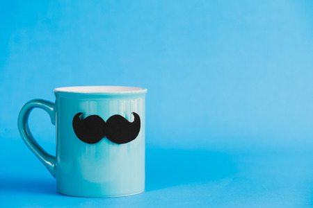Happy fathers day concept. mustache and bow tie on cyan pastel coffee cup on blue background.の写真素材