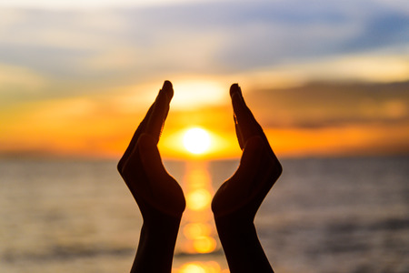Woman hands holding the sun during sunrise or sunset.の写真素材