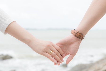 Symbols of love. Couple of man and woman hand holding together on blurred sea and sky background for love and valentines day conceptの写真素材