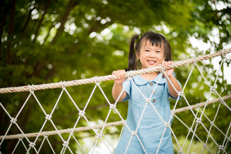 Happy little girl playing climbing on the rope bridge in adventure park colorful garden on hot summer day. Summer activities for kids.の写真素材