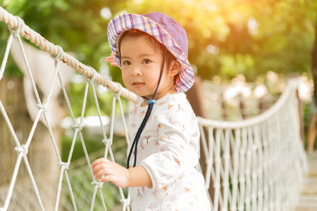 Happy little girl playing climbing on the rope bridge in adventure park colorful garden on hot summer day. Summer activities for kids.の写真素材