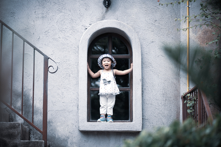 Happy cute little girl smiling and standing by the window with vintage color tone.の写真素材