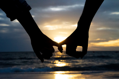 Symbols of love. silhouette Couple of man and woman hand holding together on sea and sky background during sunset for friendship day, love and valentines day conceptの写真素材