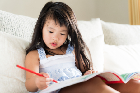 Happy cute little girl smiling and holding red pencil and drawing, writing on a book to do homework. kid education concept.の写真素材