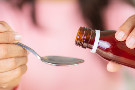 Woman hand pouring medication or antipyretic syrup from bottle to spoon. healthcare, people and medicine concept.の写真素材