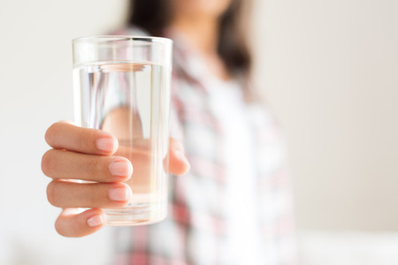 Happy beautiful young woman holding drinking water glass in her hand. Health care concept.