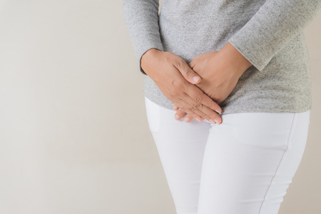 Young woman having painful stomachache with hands holding pressing her crotch lower abdomen. Medical or gynecological problems, healthcare conceptの写真素材