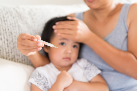Close up of a mother checking the temperature of her ill baby with a thermometer on a couch in the living room at home. Medicine and health care concept.の写真素材