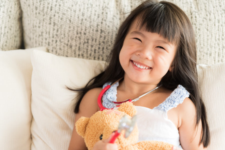 Cute little girl is smiling and playing doctor with stethoscope and teddy bear. Kid and health care concept.の写真素材