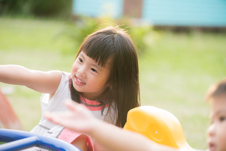 Happy little girl having fun on a playground enjoying a swing ride on a hot summer day in a sunny city park.の写真素材