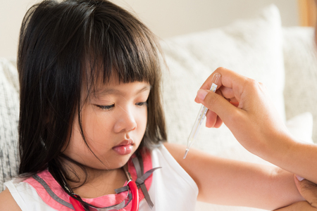 Doctor holding digital thermometer to measuring temperature of her ill kid and sick little girl with stethoscope in background.の写真素材