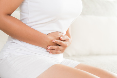 Young woman having painful stomachache sitting on sofa at home. Chronic gastritis. Abdomen bloating concept.の写真素材