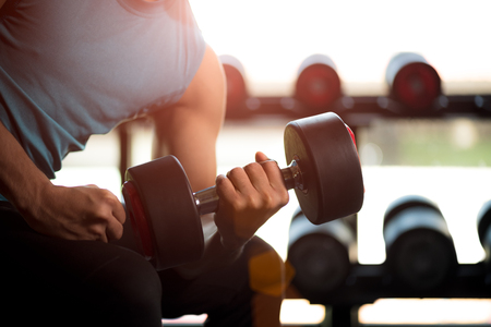 Man hand holding dumbbell exercise in gym. Fitness muscular body with set of black weights in the gym background. exercise and healthy lifestyle concept.の写真素材