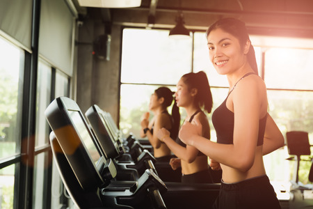 Happy asian woman with group of young people running or jogging on treadmills in modern sport gym. exercise and sport concept.の写真素材