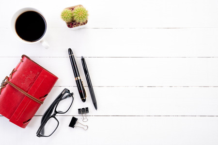 White wooden office desk table with red notebook, black pen, coffee cup and other office supplies. Top view with copy space, flat lay.の写真素材