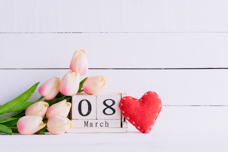 Womans day concept. Pink tulips and red heart with March 8 text on wooden block calendar on white wooden background.の写真素材