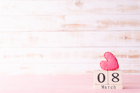 International Womens day concept. March 8 text on wooden block with handmade pink heart on white...