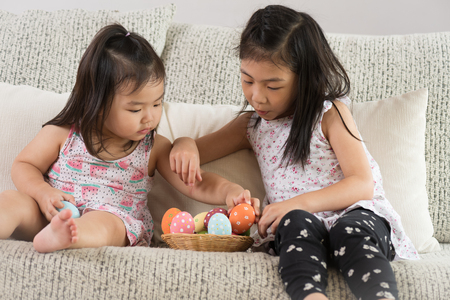 Happy easter! Two cute little children sitting on sofa with Easter eggs in the nest or basket.