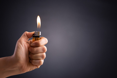Close up woman hand holding a burning lighter in the dark background.の写真素材