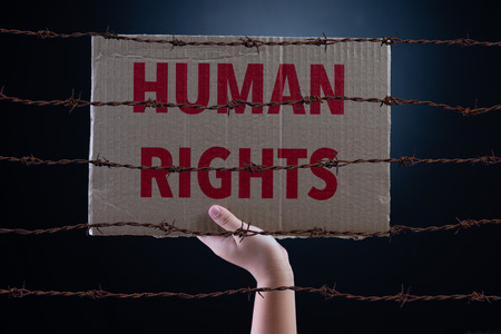 Kid hand holding cardboard paper with HUMAN RIGHTS text and rusty sharp bare wire on dark...